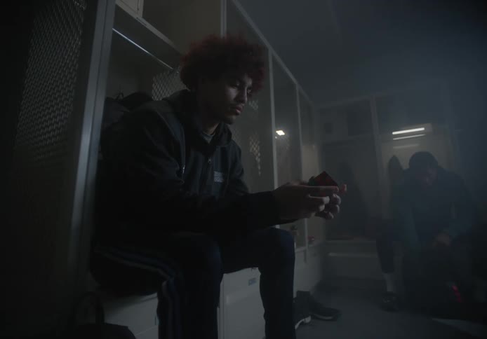 A young man sits in a locker room while playing with a rubiks cube