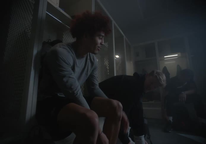 A group of men sit down in a locker room and begin to remove their shoes