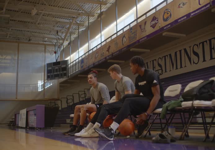 Three young basketball players sit while practicing their dribbling skills
