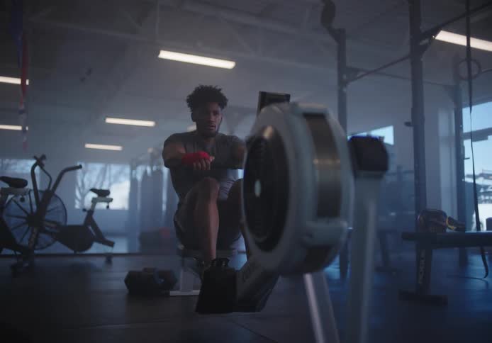 A man exercises on a rowing machine in a gym during the day