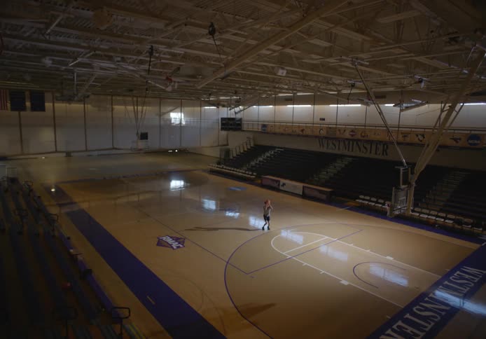 A lone basketball player practices shooting in a darkened gym