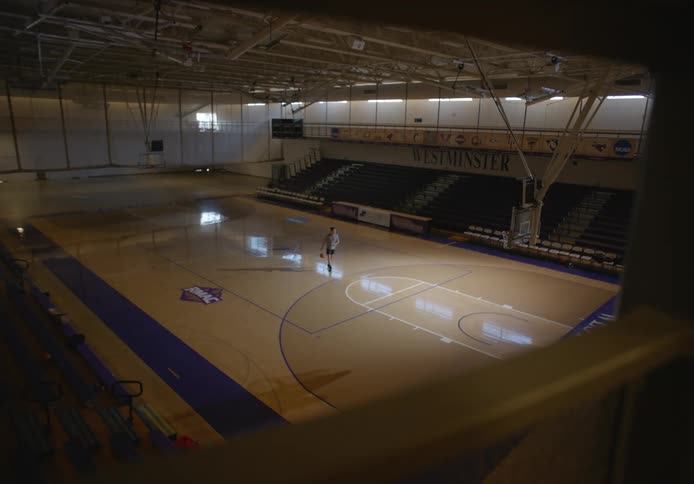 A lone basketball player practices his jump shot in an empty gymnasium