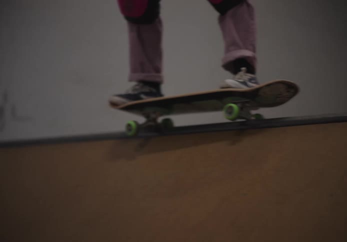 Girl wearing a safety helmet and knee pads skateboarding on an indoor skate park
