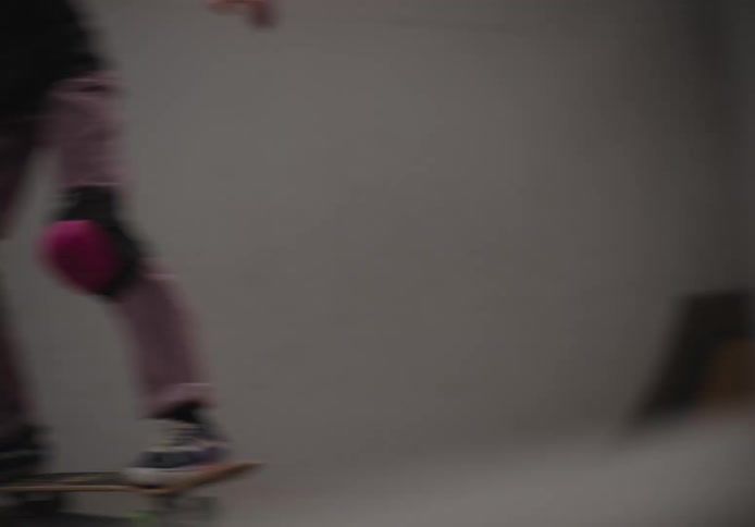 Girl with a helmet and knee pads practicing skateboarding on an indoor skate park