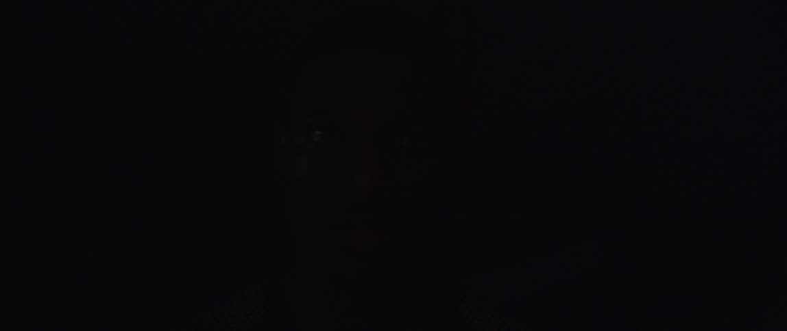 Black mans face in a dark room with a light casting alternating shadows on his face