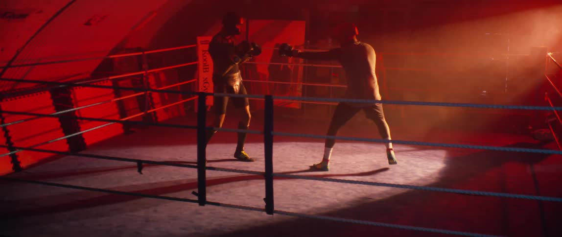 Two men are sparring in a boxing ring with a red light background