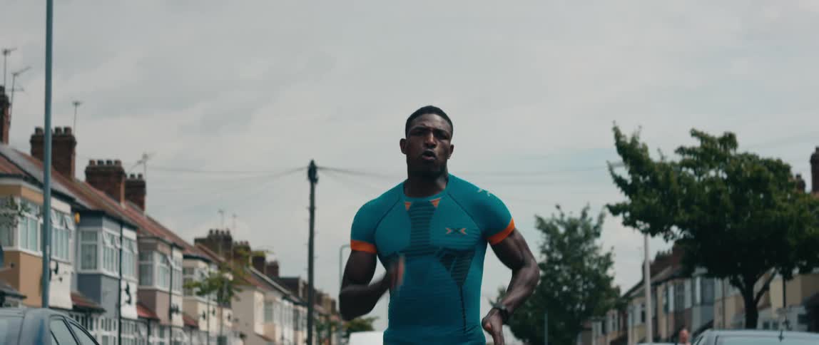 A man in athletic wear runs down the street in a residential neighborhood on a cloudy day