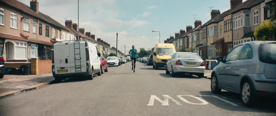 A man jogs down the street in a residential neighborhood during the day