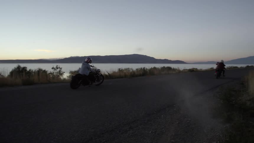 A person rides a motorcycle down the road at sunset