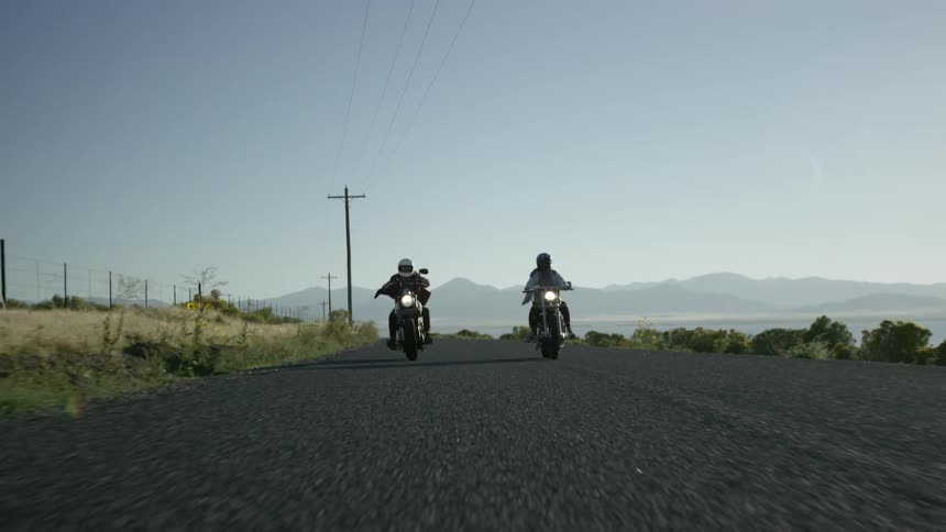 Two people ride on a road with motorcycles
