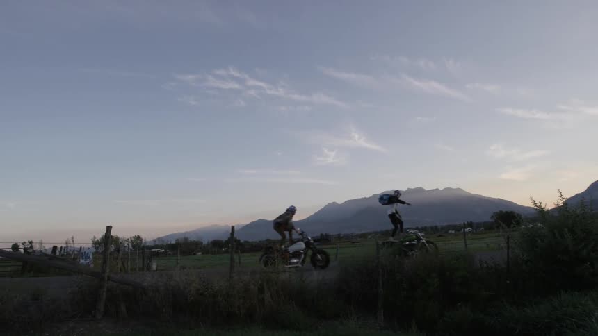 People riding standing up on motorcycles after sunset