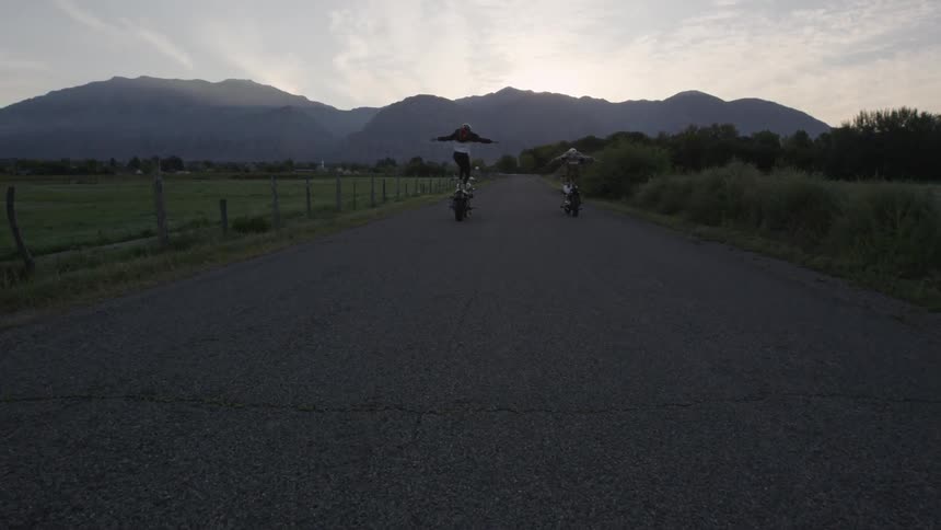 Two motorcyclists standing on their bikes as they ride down a road