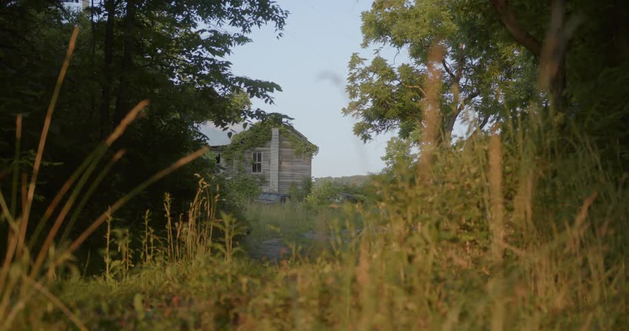 An old looking house is being spied on through an opening in the woods across from it