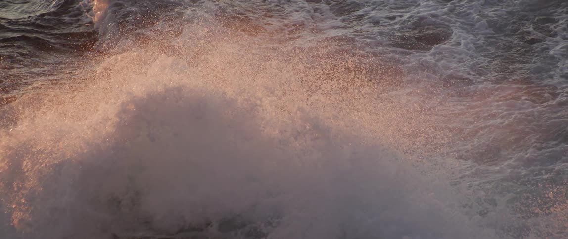 A wave crashes in the ocean during the day
