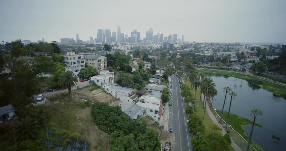 An aerial view of a hillside suburb with a lake across the street and a large metropolis in the background