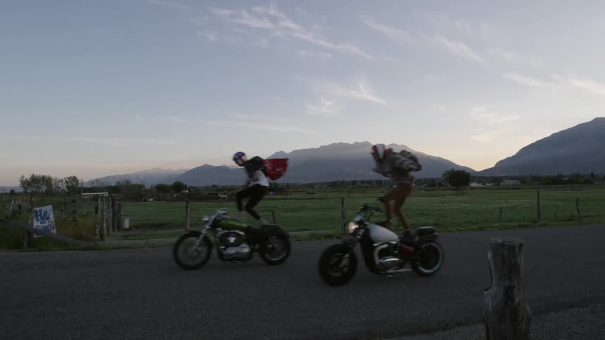 Two people doing a trick standing on their moving motorcycles