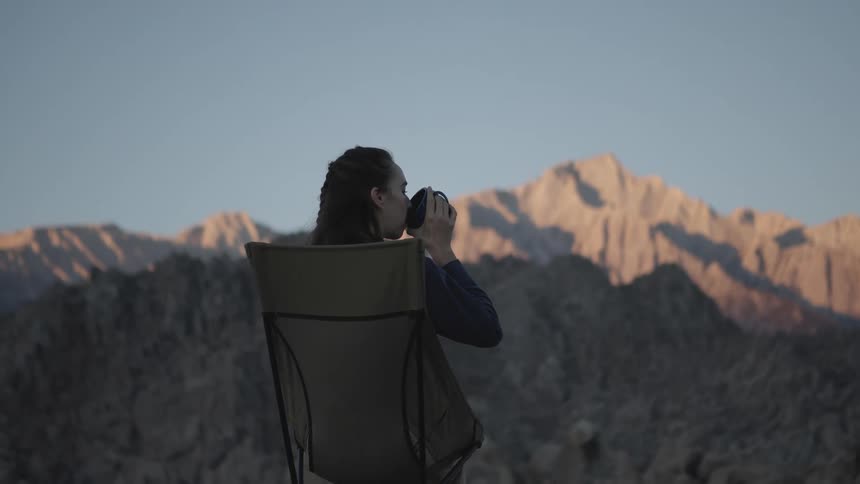 A woman is sitting on the mountain drinking