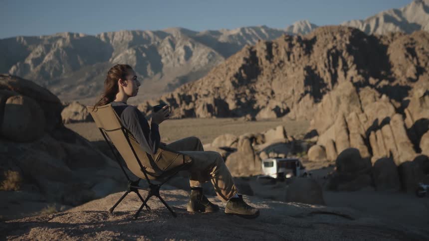 A woman camping out of her van drinks her morning coffee at sunrise