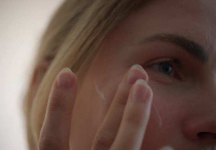 A woman is applying moisturizer to her face
