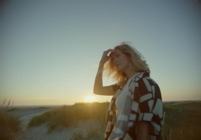 Blonde woman at an empty beach during dusk or dawn touching her hair and looking away at the ocean