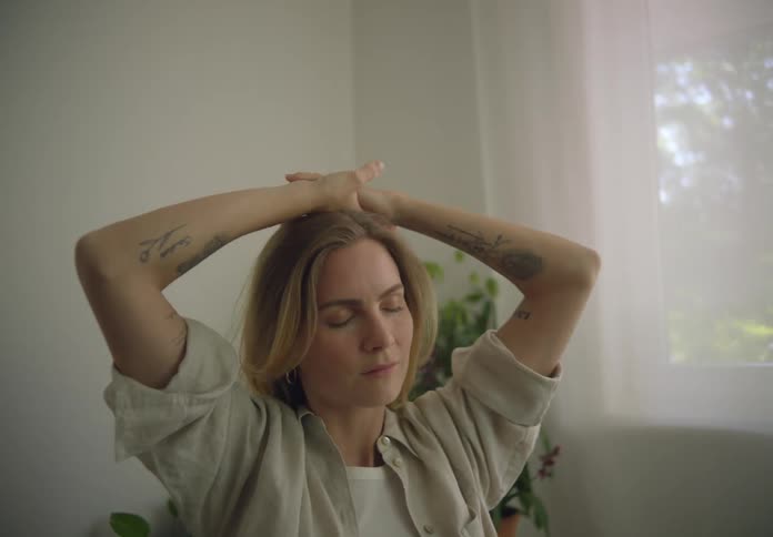 A woman stretches her arms while sitting indoors during the day