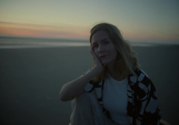 A woman looks into the camera while posing on a chair on a beach in the evening