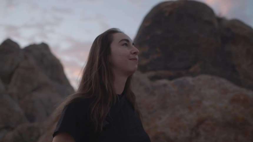 A young woman stands near large rock formations while admiring nature