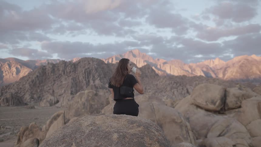 Woman dressed in black sitting in a rock outdoors drinking water