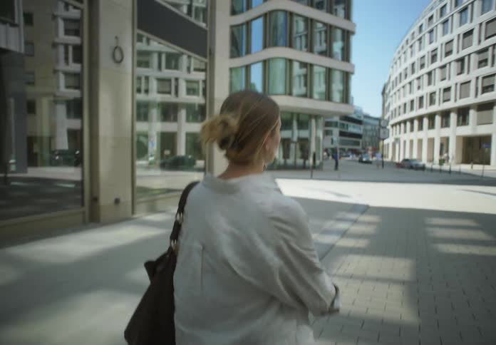 A woman glances over her shoulder as she walks through a city while holding a smartphone to her ear