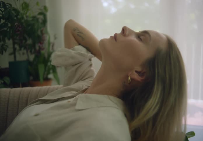 Woman leans back on couch near window and pushes her hair back