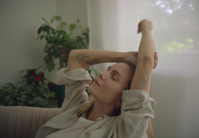 Woman seated in a cozy armchair next to the window relaxing and stretching her arms