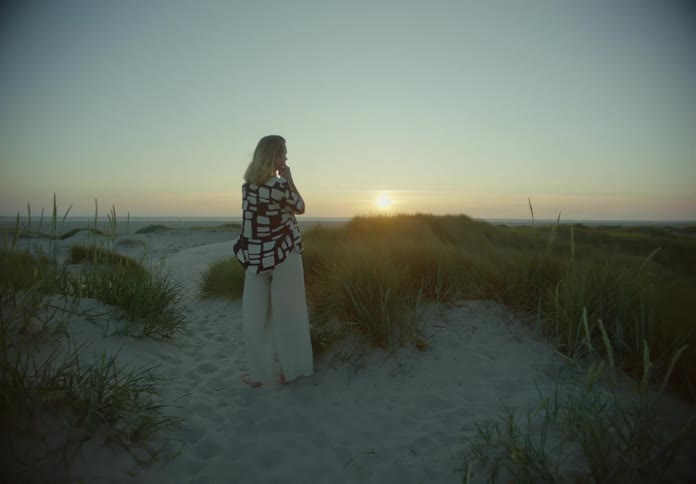 Blonde woman standing up at the beach during dusk or dawn