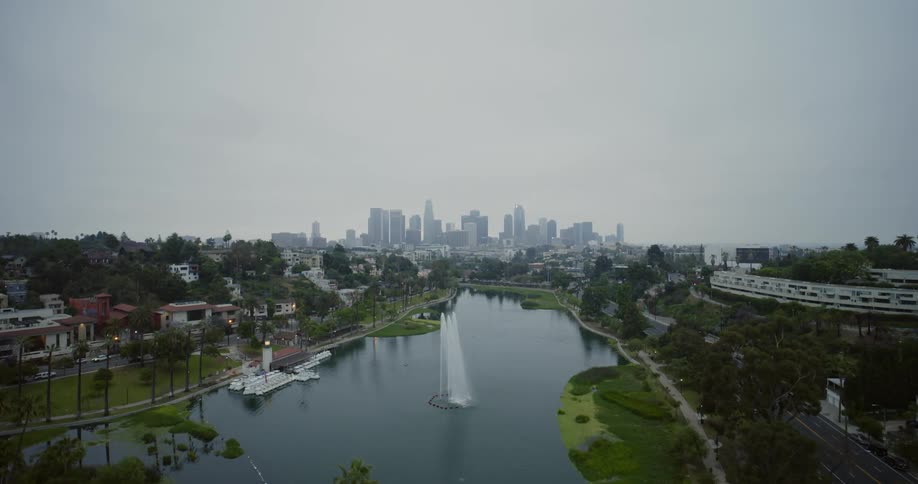 Large water fount spouts in river paralleled by highway with city skyline in the distance