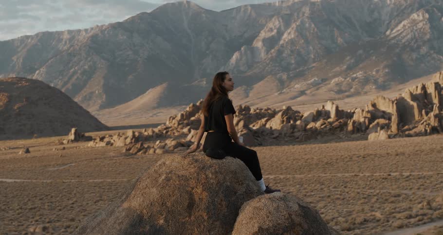 Woman sitting on a rock outdoors watching a chain of mountains around her