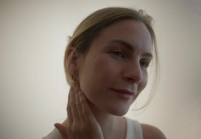 Blonde woman indoors massaging her face and neck