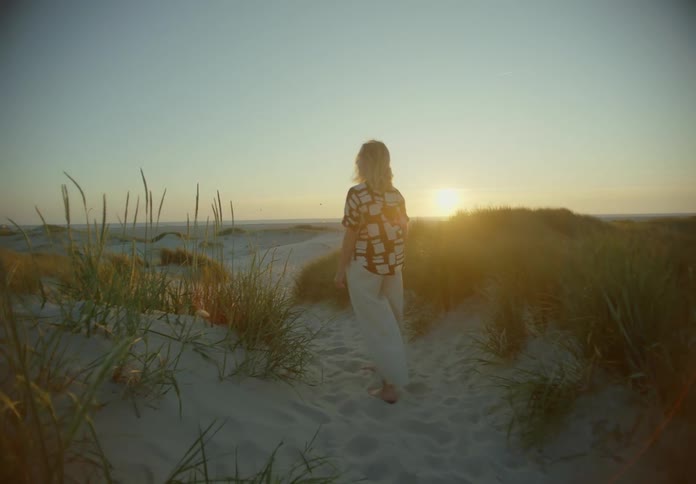 Blonde woman walking alone at a beach during dusk or dawn