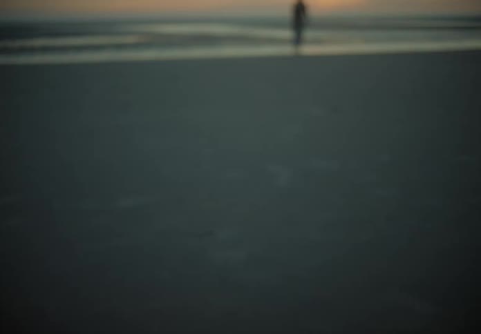 A woman is walking on the beach in the distance