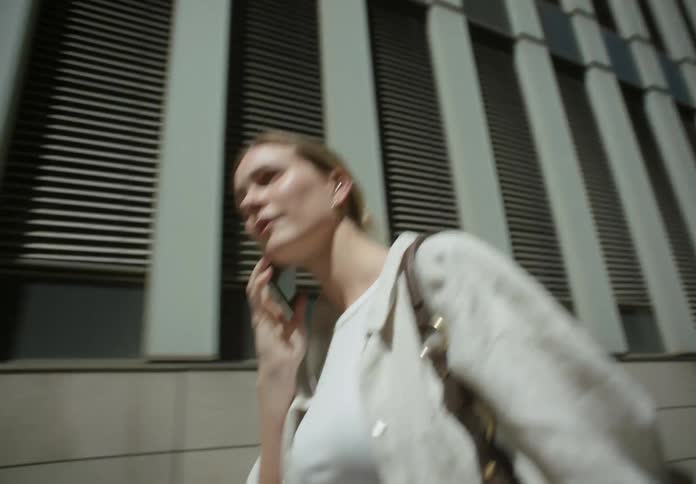 A woman makes a call on her smartphone while walking outdoors in a city during the day