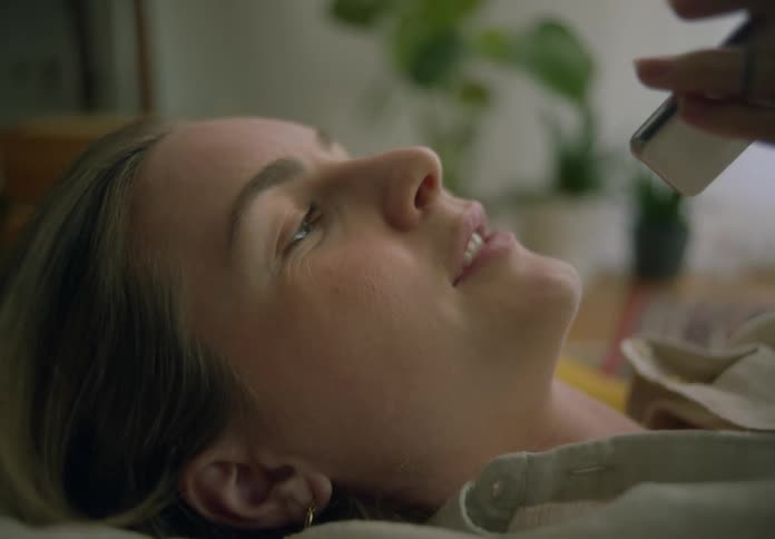 A woman speaks into her smartphone while lying down indoors during the day