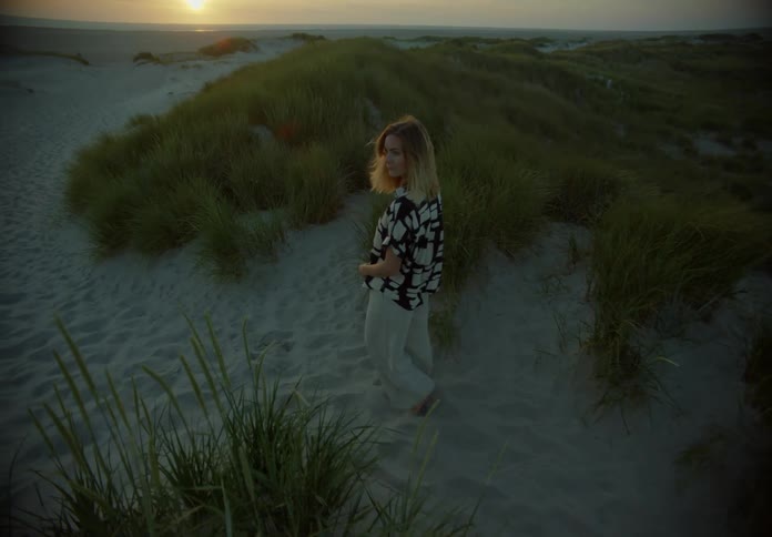 A woman is walking on the beach at sunset