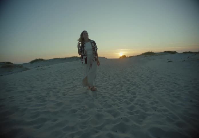 Blonde woman walking on a windy beach during dusk or dawn