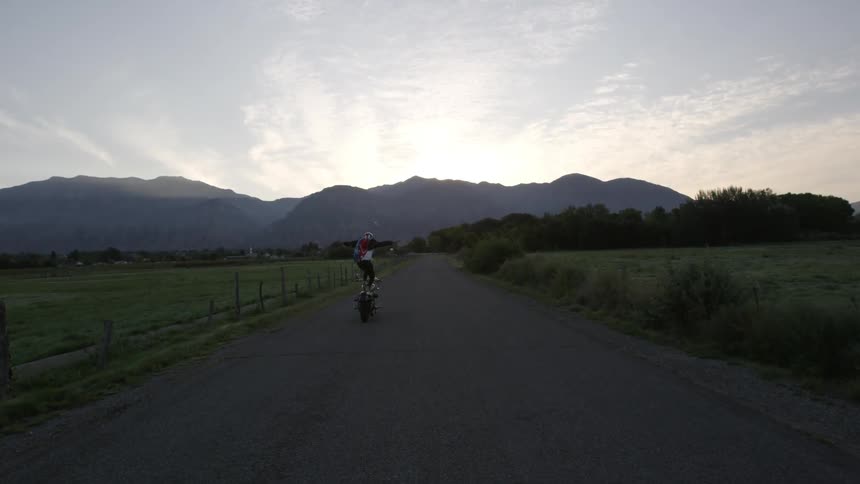 A person standing on a motorcycle races down the road