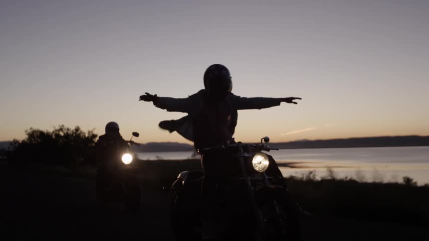A man rides standing with his arms out on a motorcycle at dawn