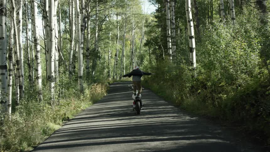 A man balances on a motorcycle in a forested area