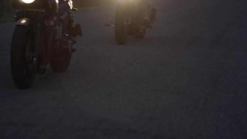 Two motorcycles drive down a dark road
