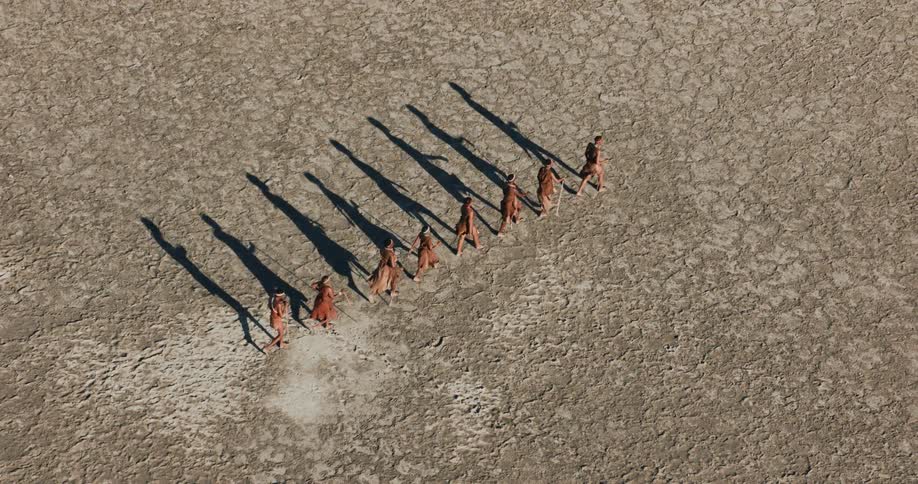 A group of bushmen hike through the salt pan in line