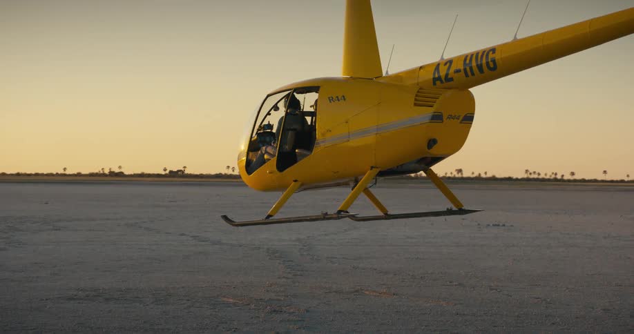 A yellow helicopter hovers over the ground as it takes off