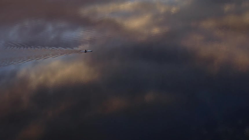 A person paddles a kayak across a placid lake that reflects the sky in the evening