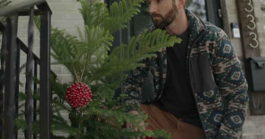 A man carefully inspects and tends to a potted plant outside his residence