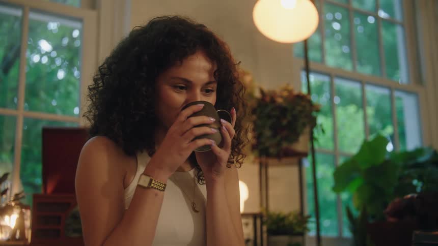 Darkhaired girl sitting at home smiling and drinking from a coffee cup